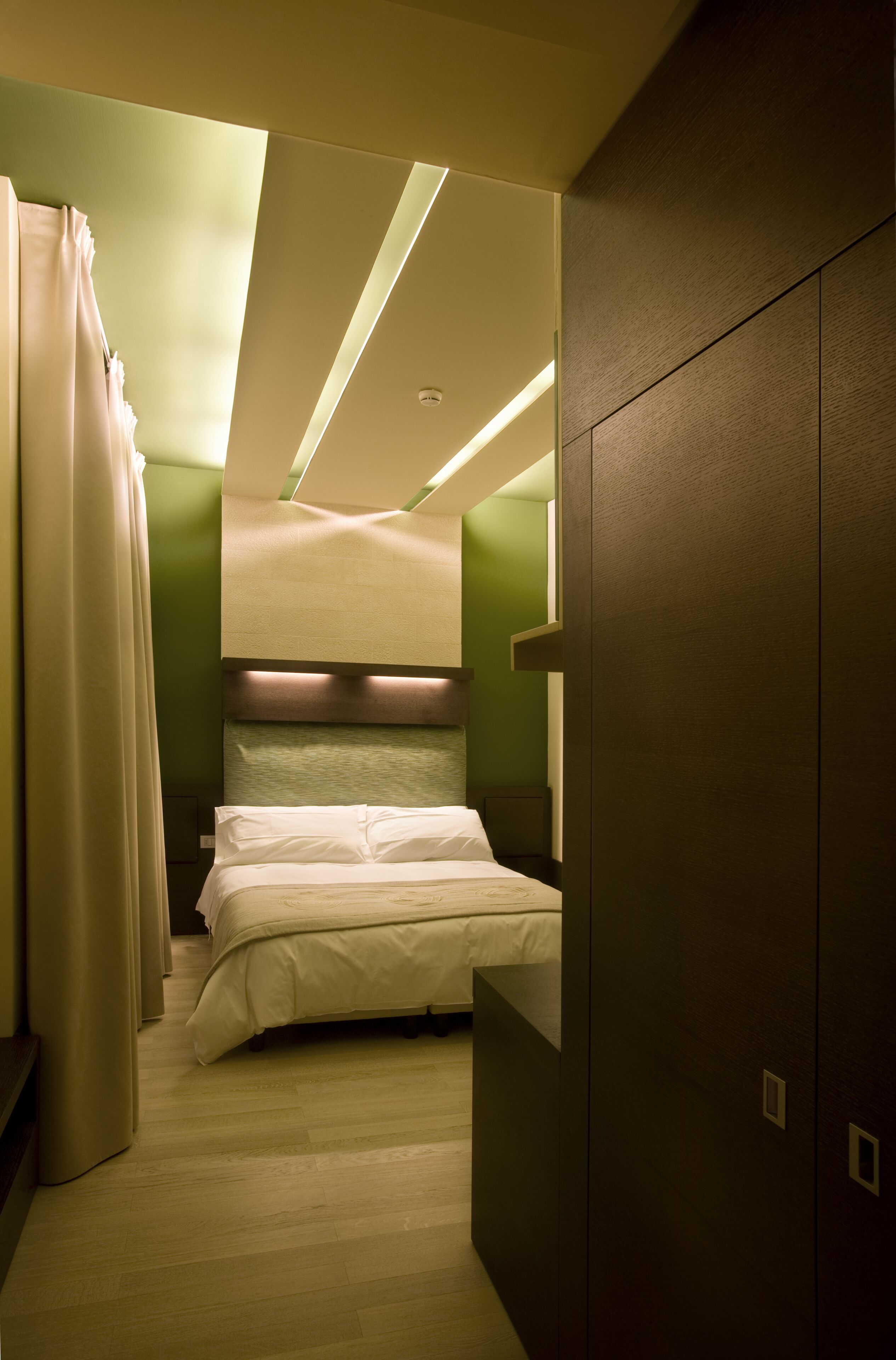 Ein Hotelzimmer mit Bett, Kopfstütze, Kleiderschrank und Vorhang.