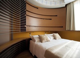 Ein modernes Schlafzimmer mit gewölbter Decke, integrierten Regalen, einem Bett mit beiger Decke und einem Fenster mit Vorhängen.
