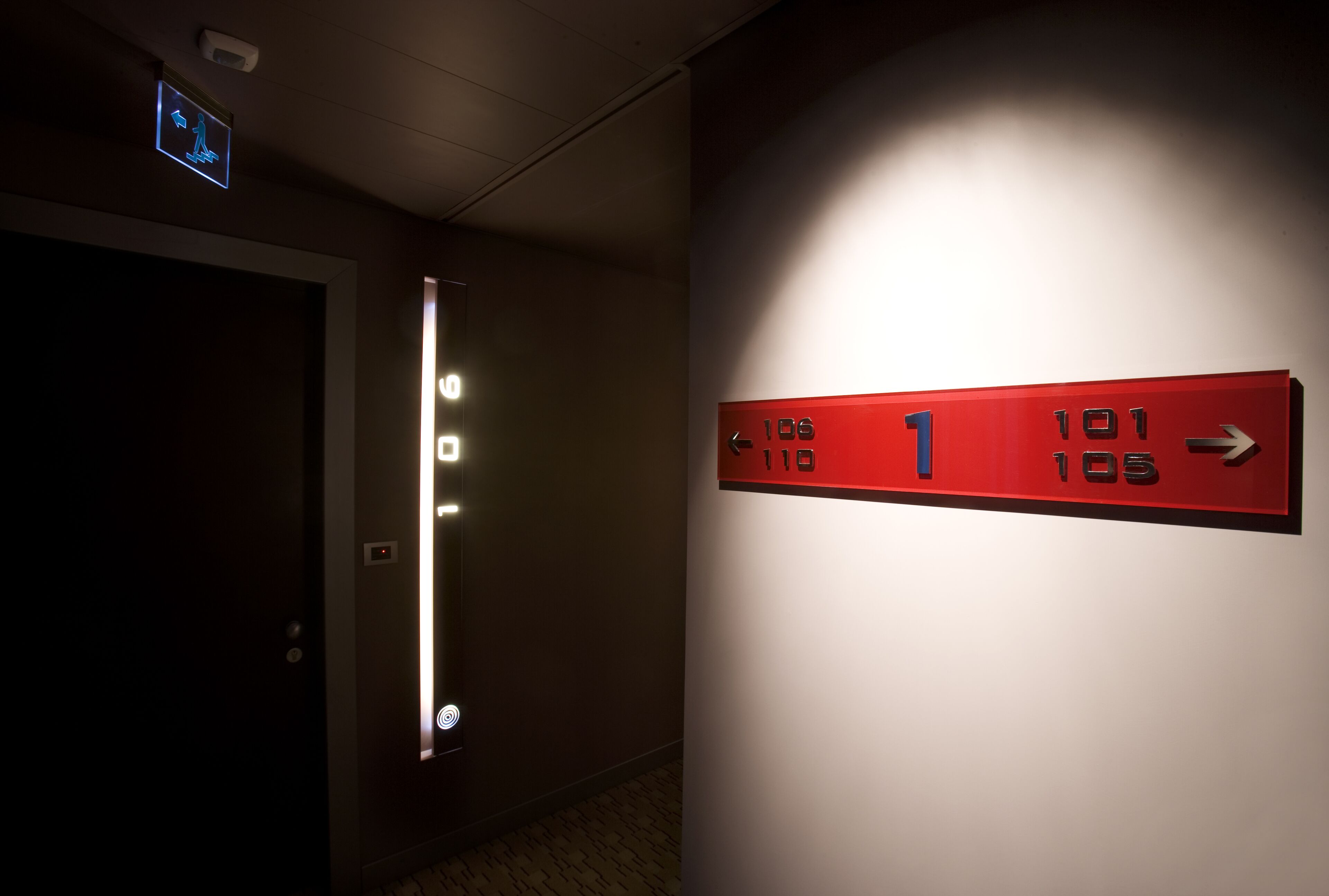 Un ascensor con indicadores iluminados del piso y una señal roja direccional con números y flechas.