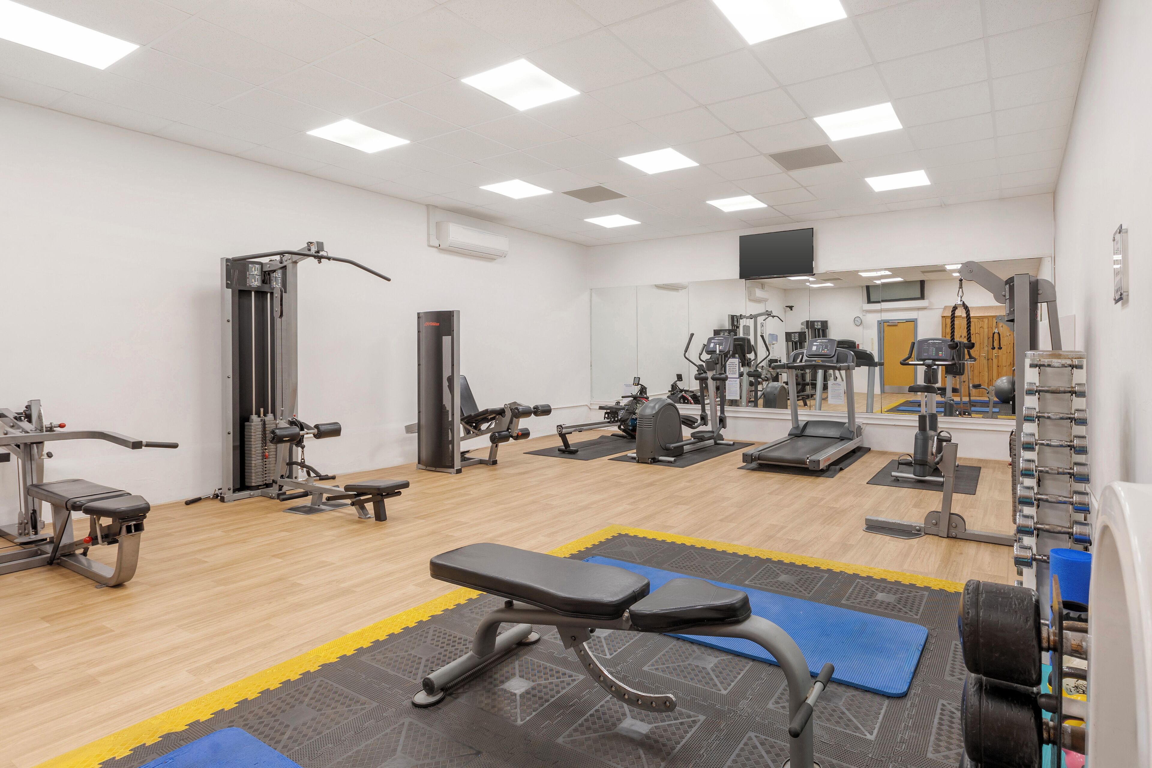 Un gimnasio con diversos equipos de ejercicio, incluyendo bancos, cintas de correr y máquinas de pesas.