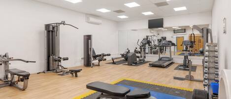 Un gimnasio con diversos equipos de ejercicio, incluyendo bancos, cintas de correr y máquinas de pesas.