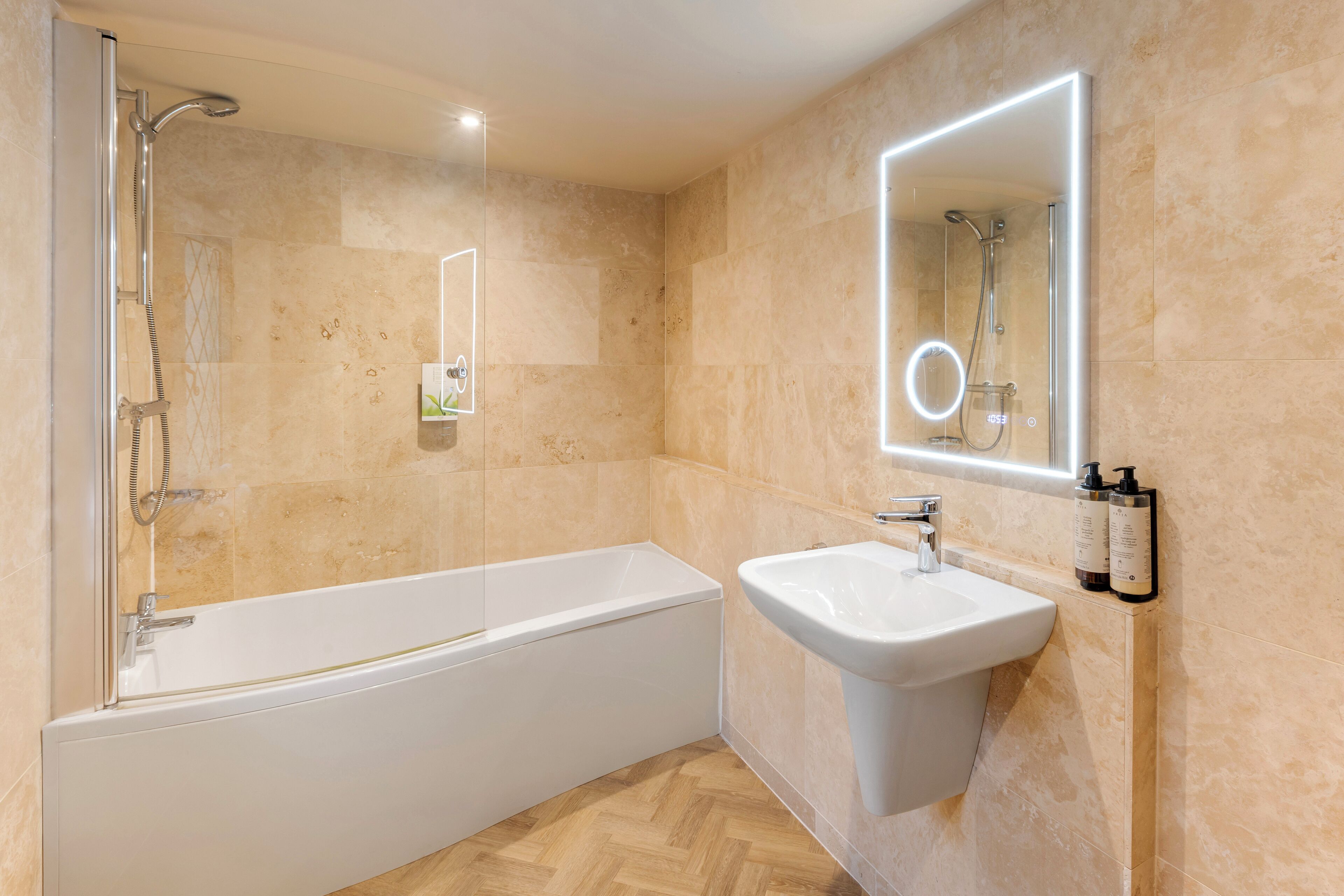 A modern bathroom with a bathtub, a sink, and a mirror with lights.