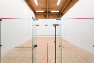 A squash court with glass walls, wooden floor, and ceiling lights.