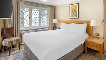 A hotel room with a large bed, two bedside tables, a chair, a window with curtains, and a painting on the wall.