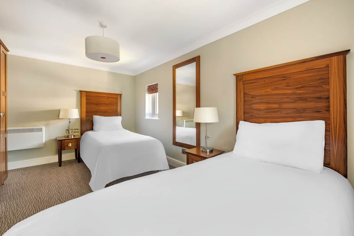 A hotel room with two beds, a large mirror, bedside lamps, a heater, and a carpeted floor.