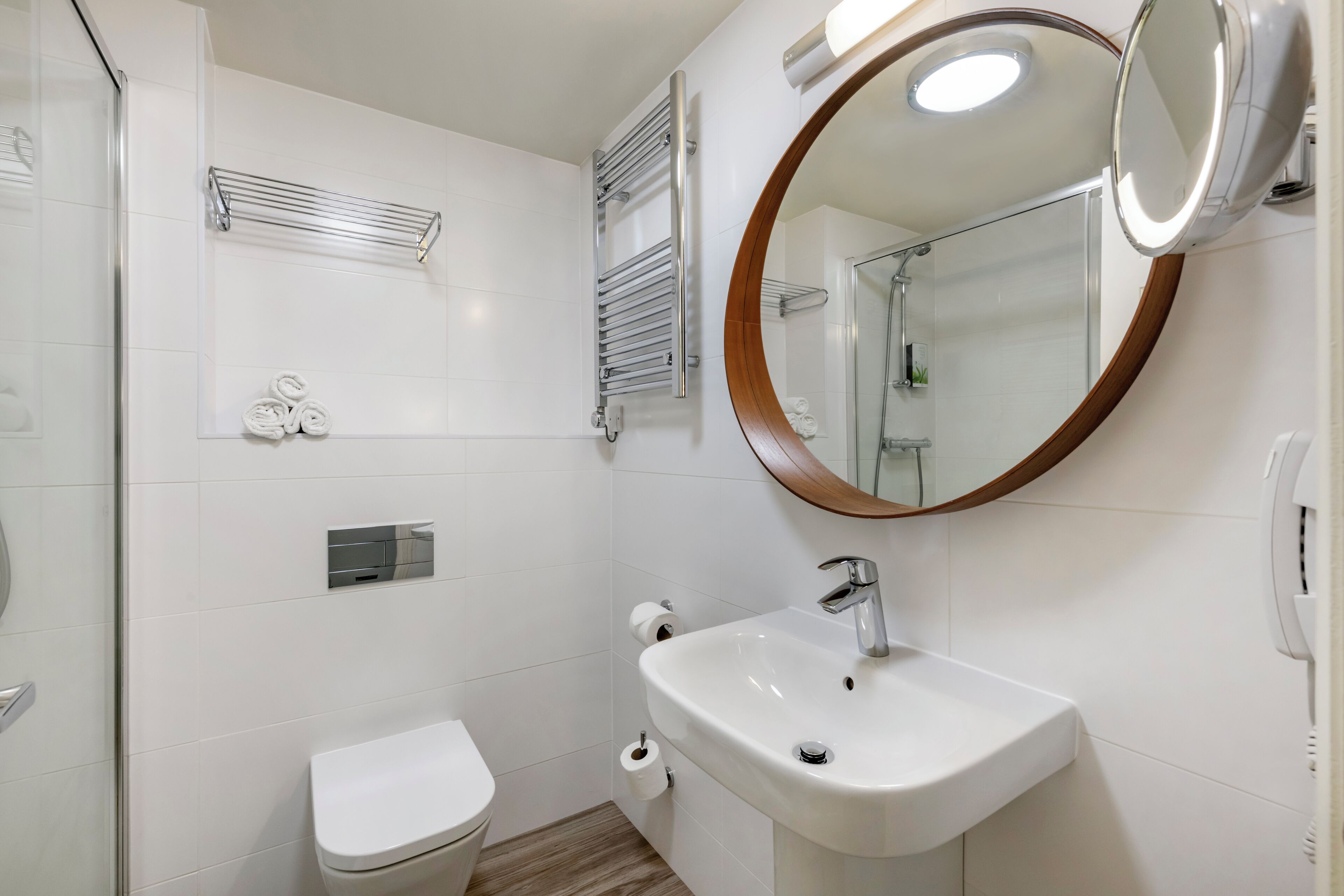 A modern bathroom with a white sink, a toilet, a shower, and a mirror with a wooden frame.