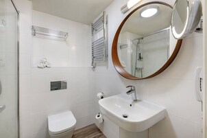 Ein modernes Badezimmer mit Waschbecken, Toilette, Dusche und einem Spiegel mit Holzrahmen.