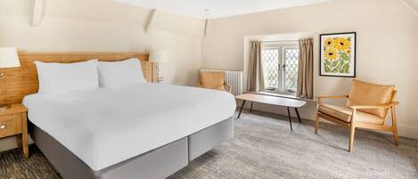 A hotel room with a large bed, a small table, a chair, a radiator, and a window with curtains.