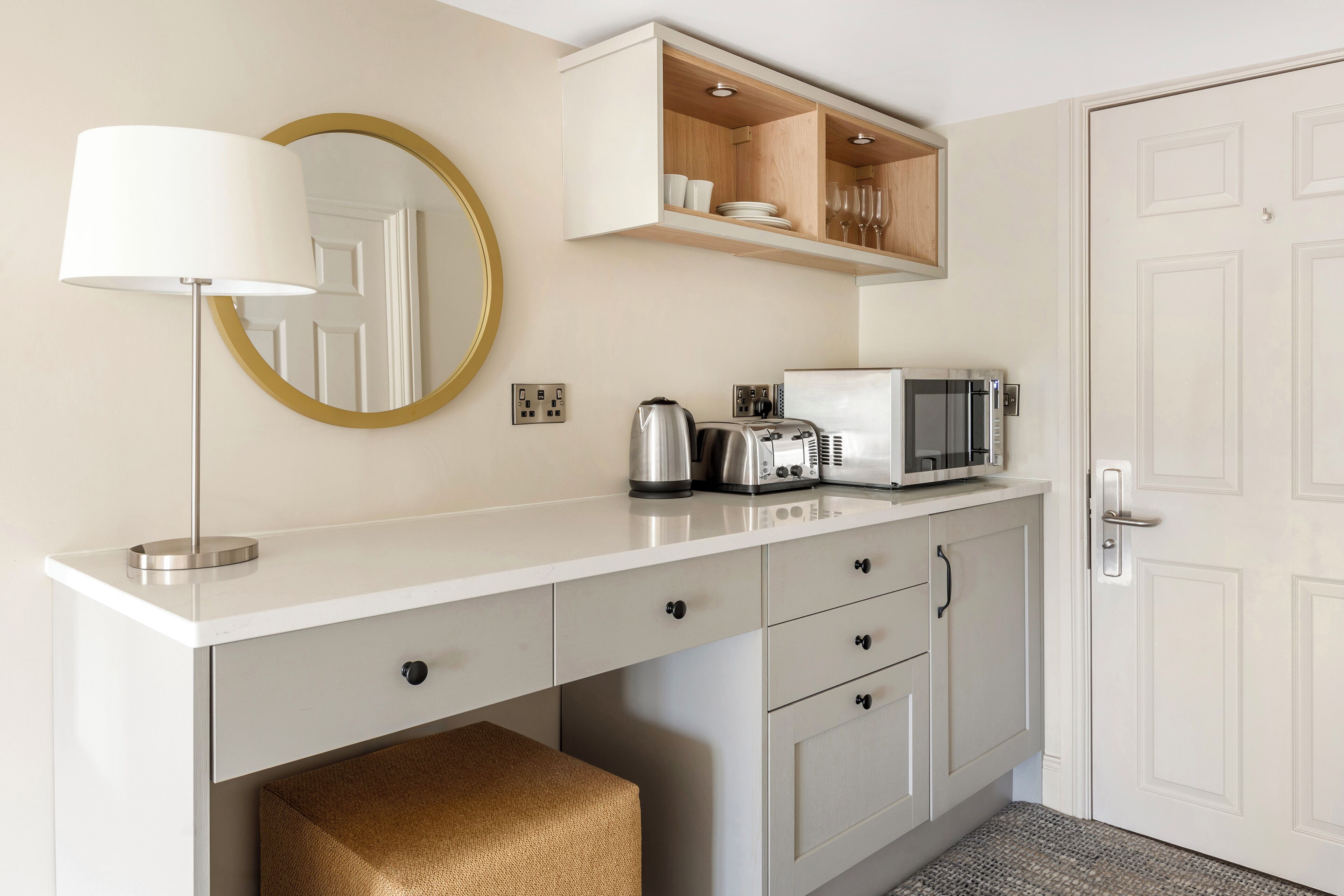 A modern kitchen with a white countertop, a kettle, a toaster, a microwave, and a cabinet above the counter.