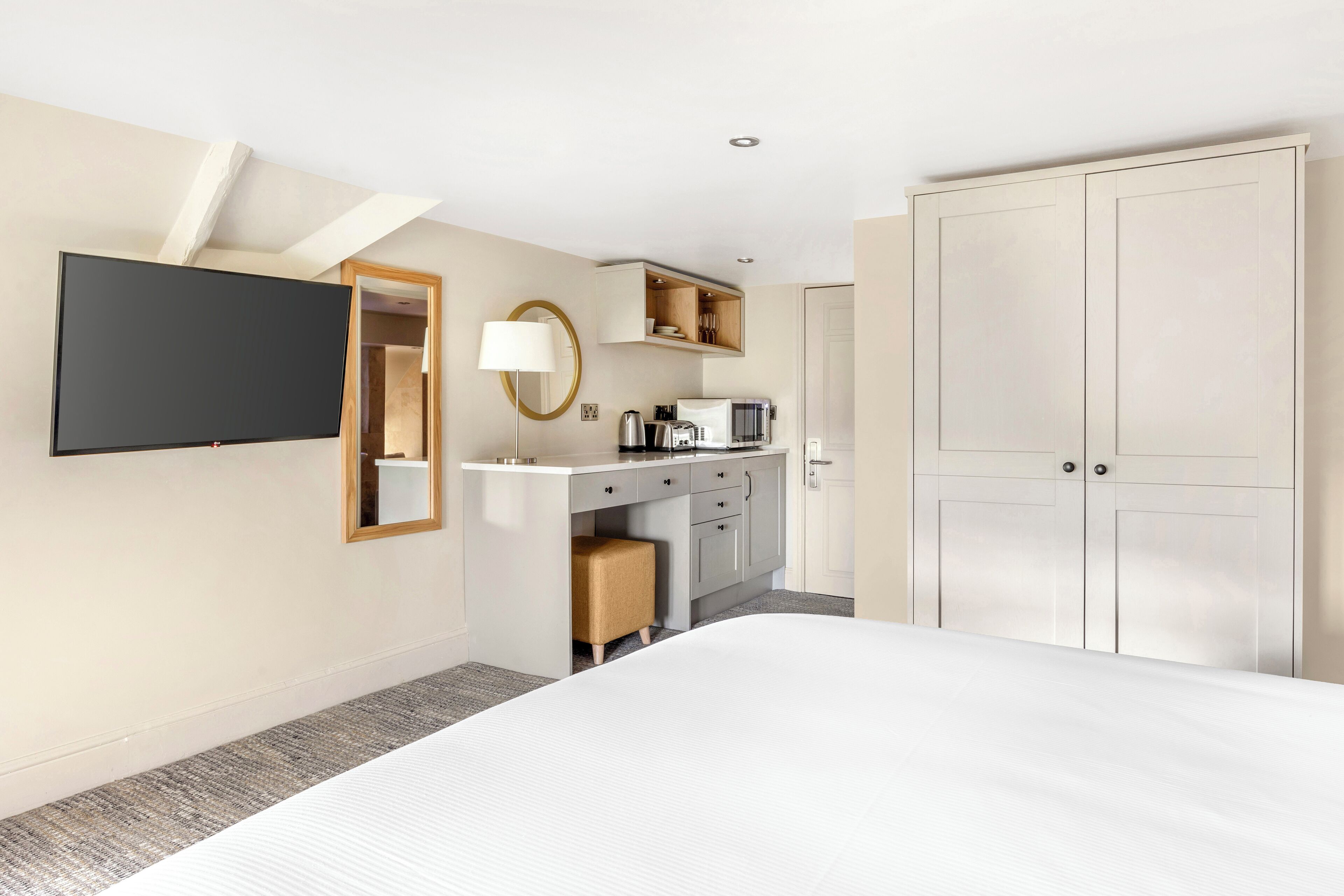 Une chambre d’hôtel comprenant un lit, un bureau avec un téléviseur à écran plat, une lampe, une kitchenette et une armoire.