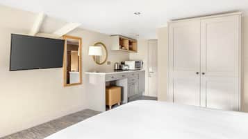 Ein Hotelzimmer mit Bett, Schreibtisch, Flachbildfernseher, Lampe, Küchenzeile und Kleiderschrank.