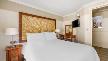Habitación de hotel con una cama grande, dos mesitas de noche con lámparas, un televisor de pantalla plana montado en la pared y un cabecero de madera con diseño de árbol.