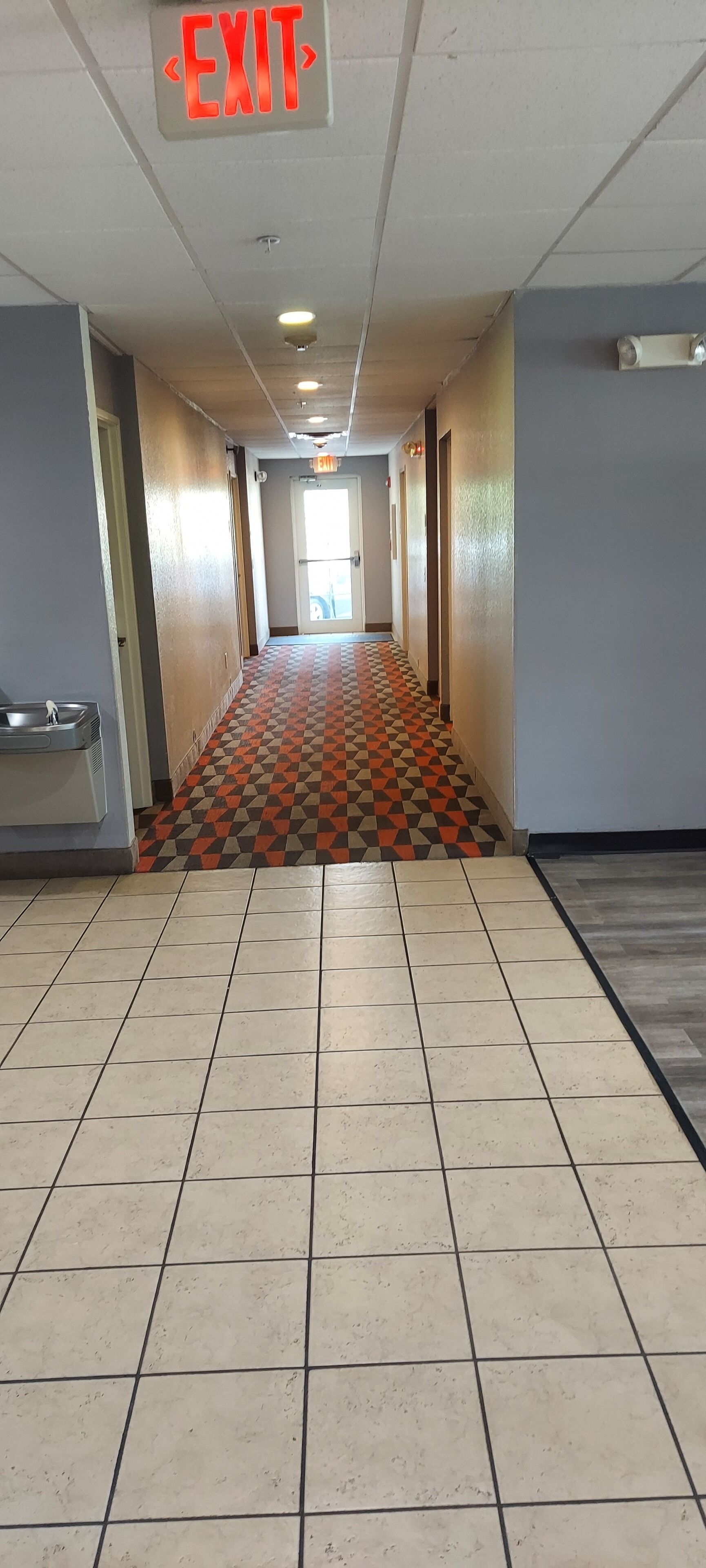 A hallway with a patterned floor, an exit sign, and a door at the end.