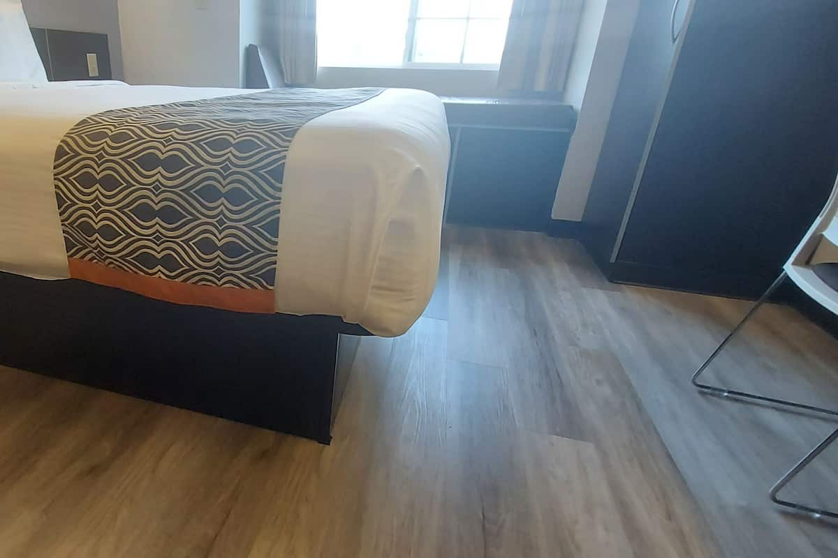 A hotel room with a bed, a window, and a wooden floor.