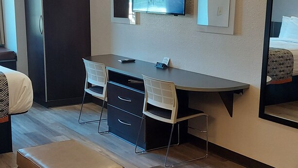 A modern hotel room with a wooden floor, a desk with two chairs, a large mirror, and a TV mounted on the wall. - Microtel Inn & Suites by Wyndham Hoover/Birmingham (Birmingham)
