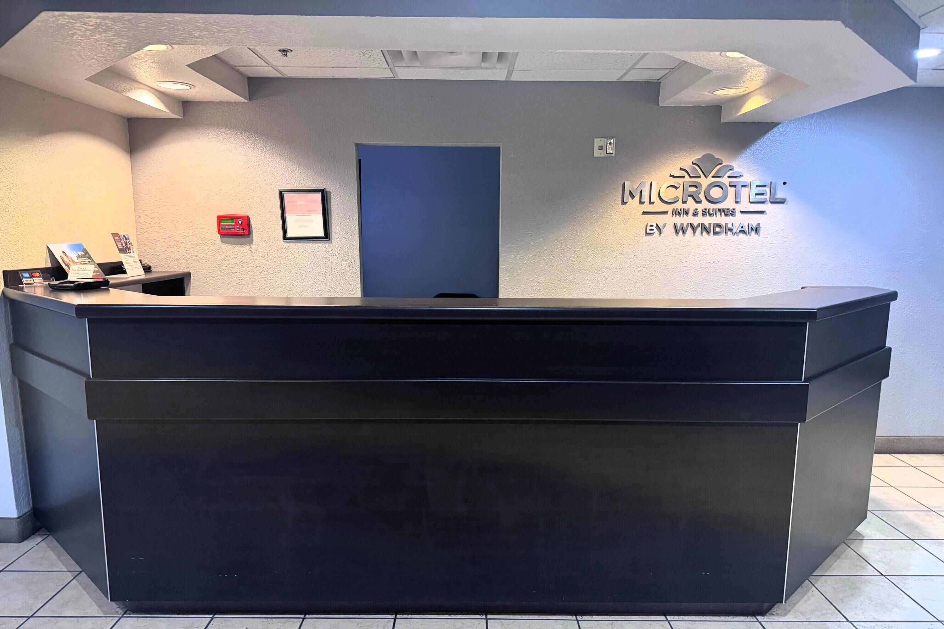 A reception desk with a dark surface, a framed picture above it, and a sign for 'MICROTEL INN & SUITES BY WYNDHAM' on the wall.