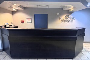 A reception desk with a dark surface, a framed picture above it, and a sign for 'MICROTEL INN & SUITES BY WYNDHAM' on the wall. - Microtel Inn & Suites by Wyndham Hoover/Birmingham (Birmingham)