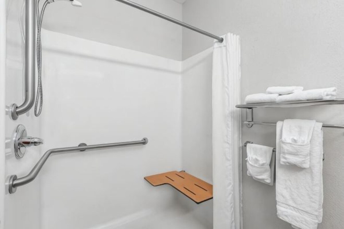A shower area with a glass door, a handrail, a towel rack with towels, and a wooden shelf.
