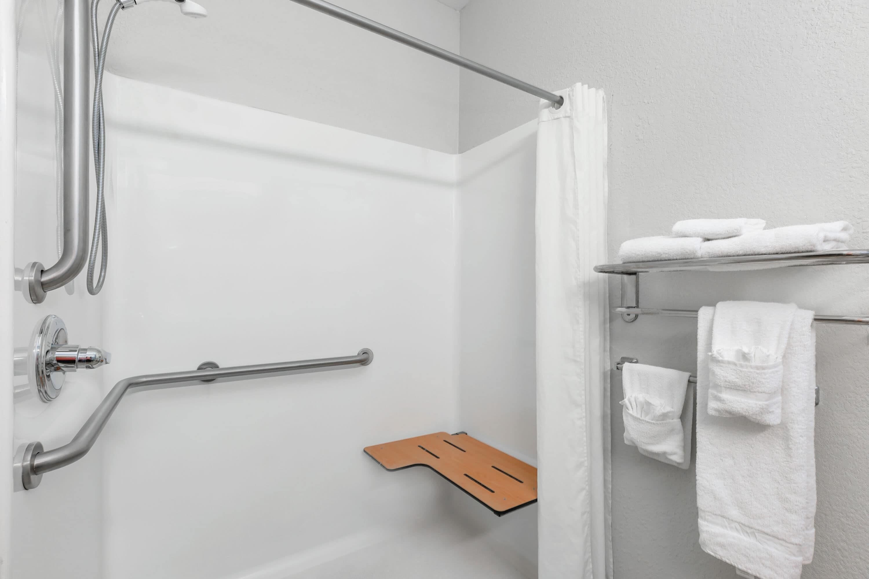 A shower area with a grab bar, a towel rack with towels, and a shower control panel.