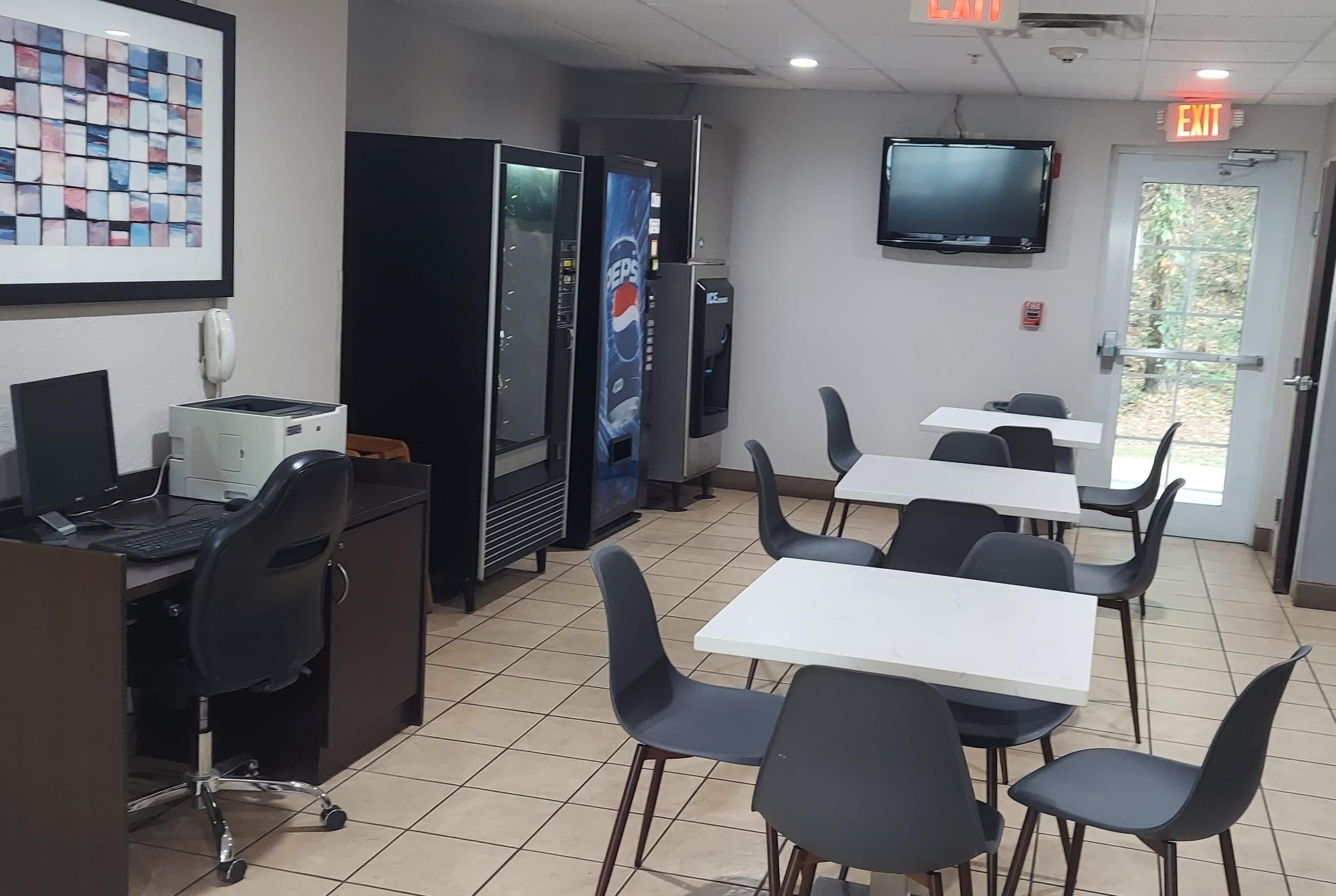 A room with a computer, a refrigerator, a television, and a door with an exit sign.