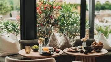 Un comedor con mesas redondas, vistas a zonas verdes y una variedad de comida y bebidas.