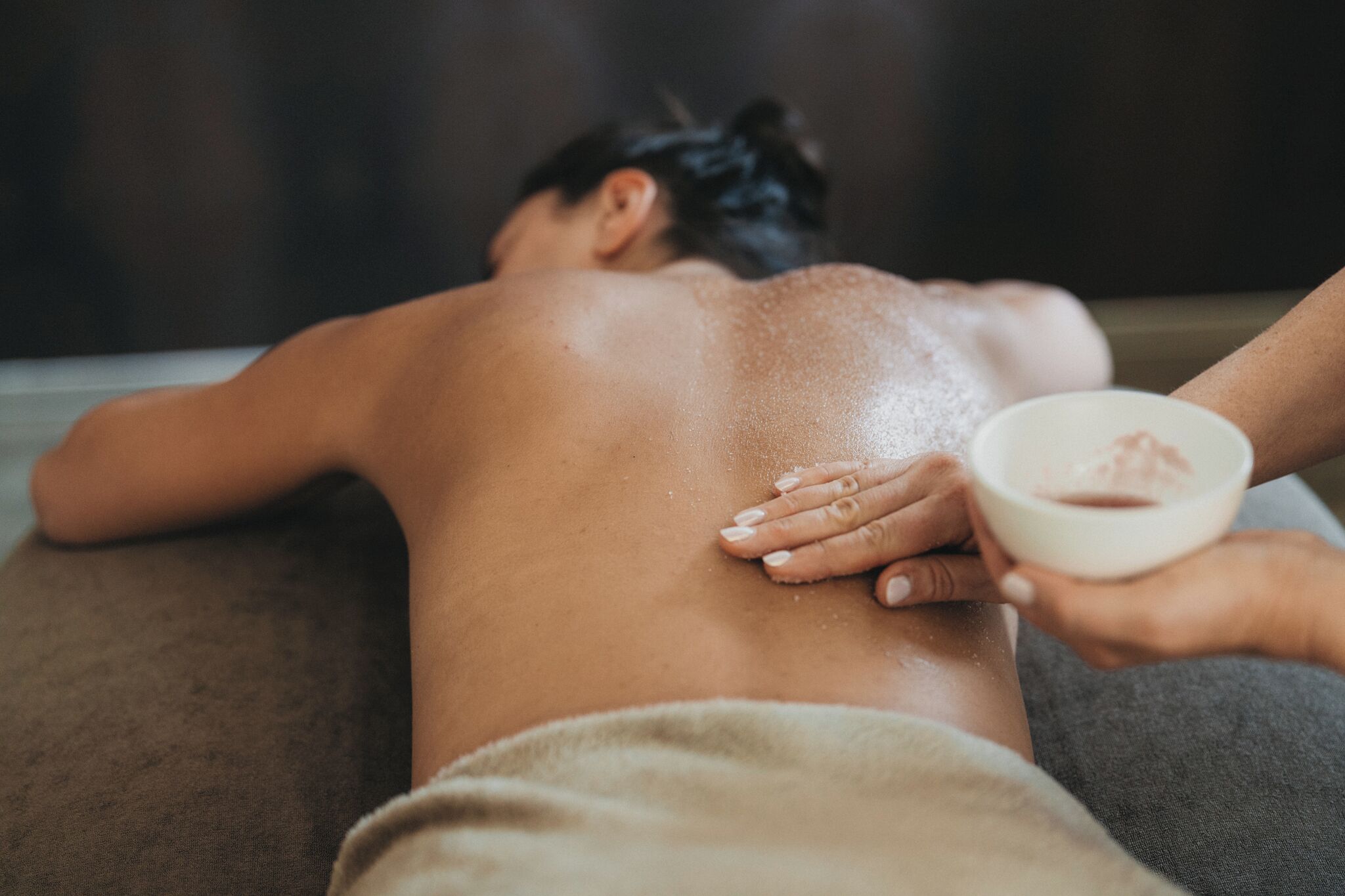 A person receiving a back massage with a bowl of cream.