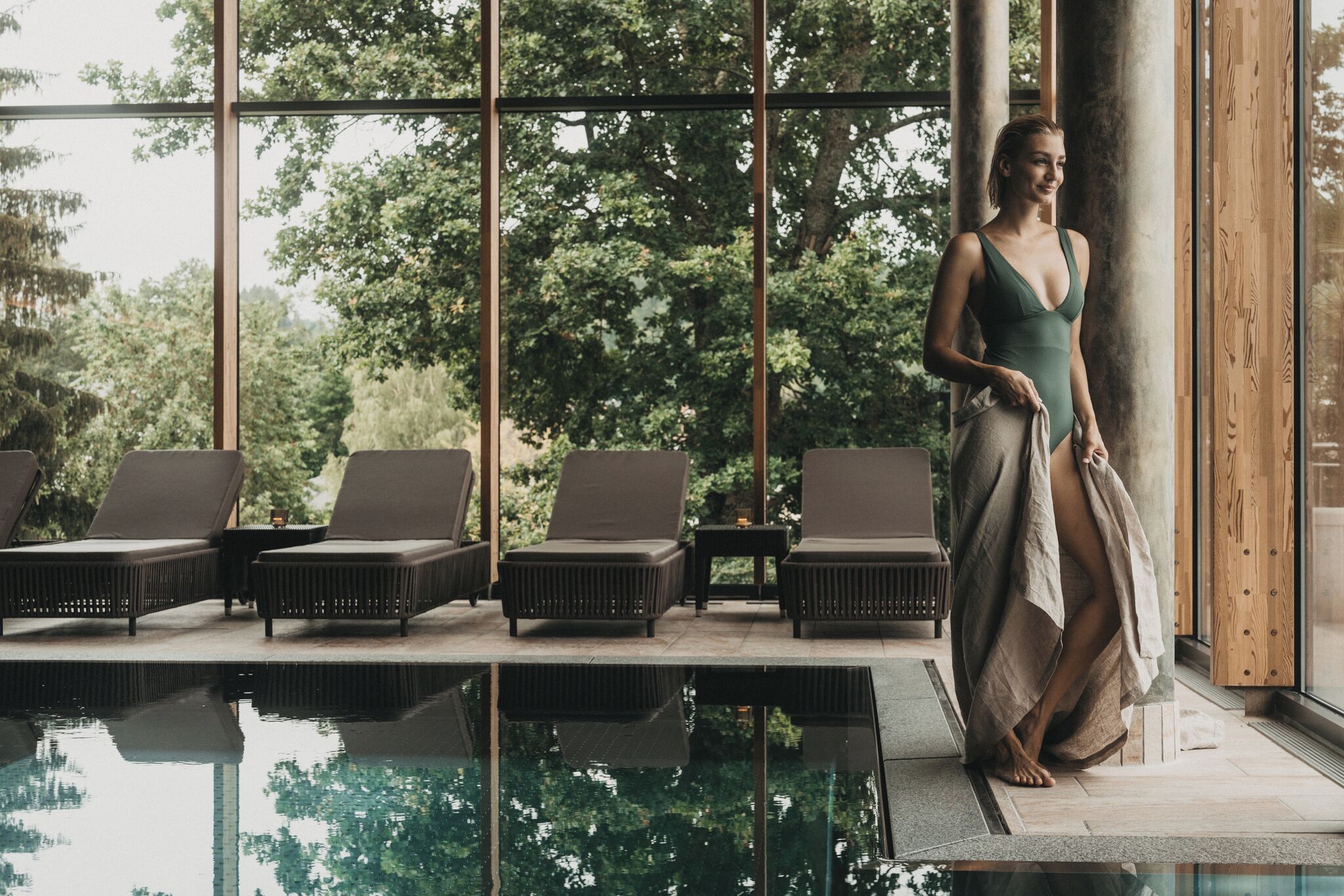 A poolside area with lounge chairs and a large window overlooking a forested area.