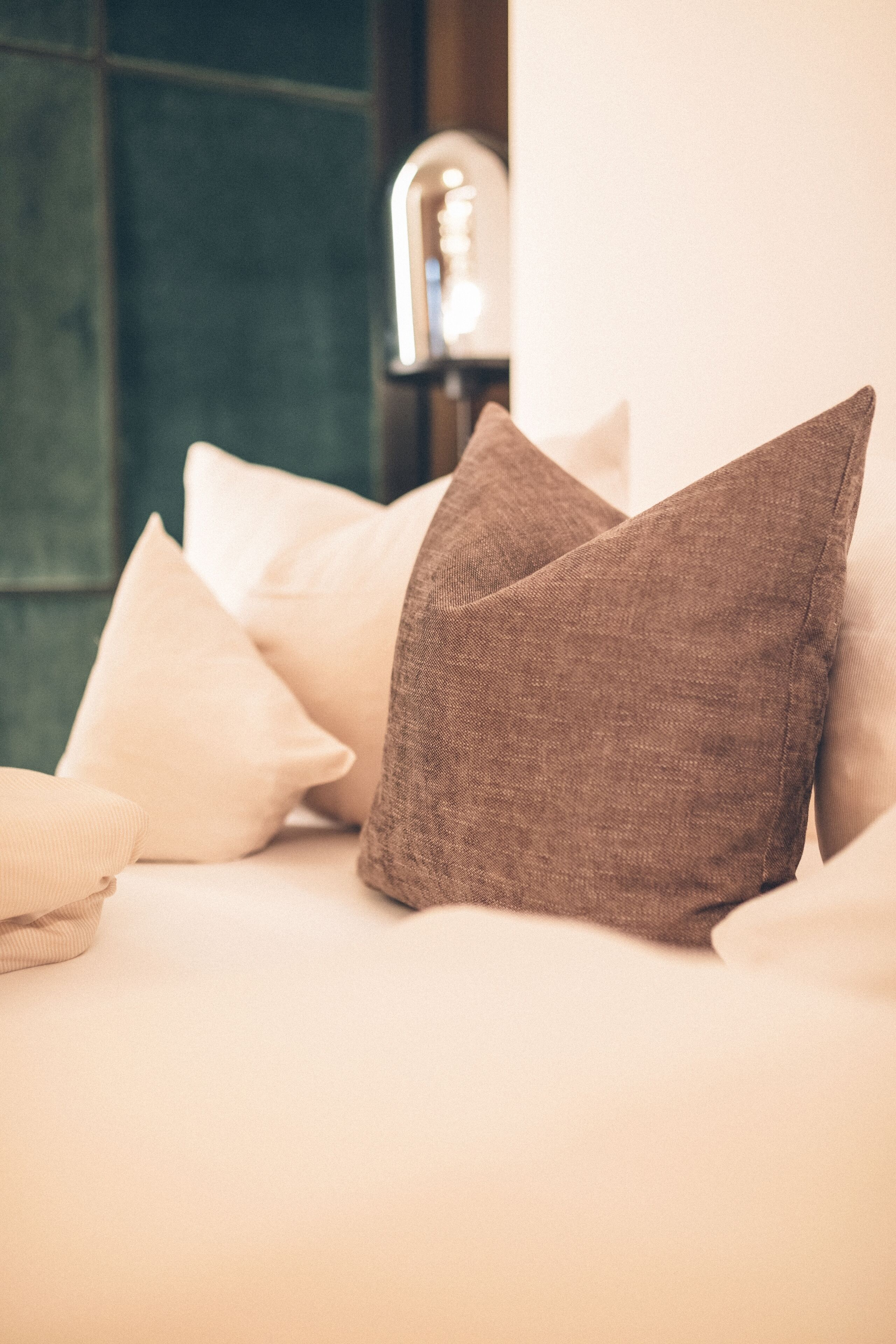 A bed with pillows and a lamp in the background.