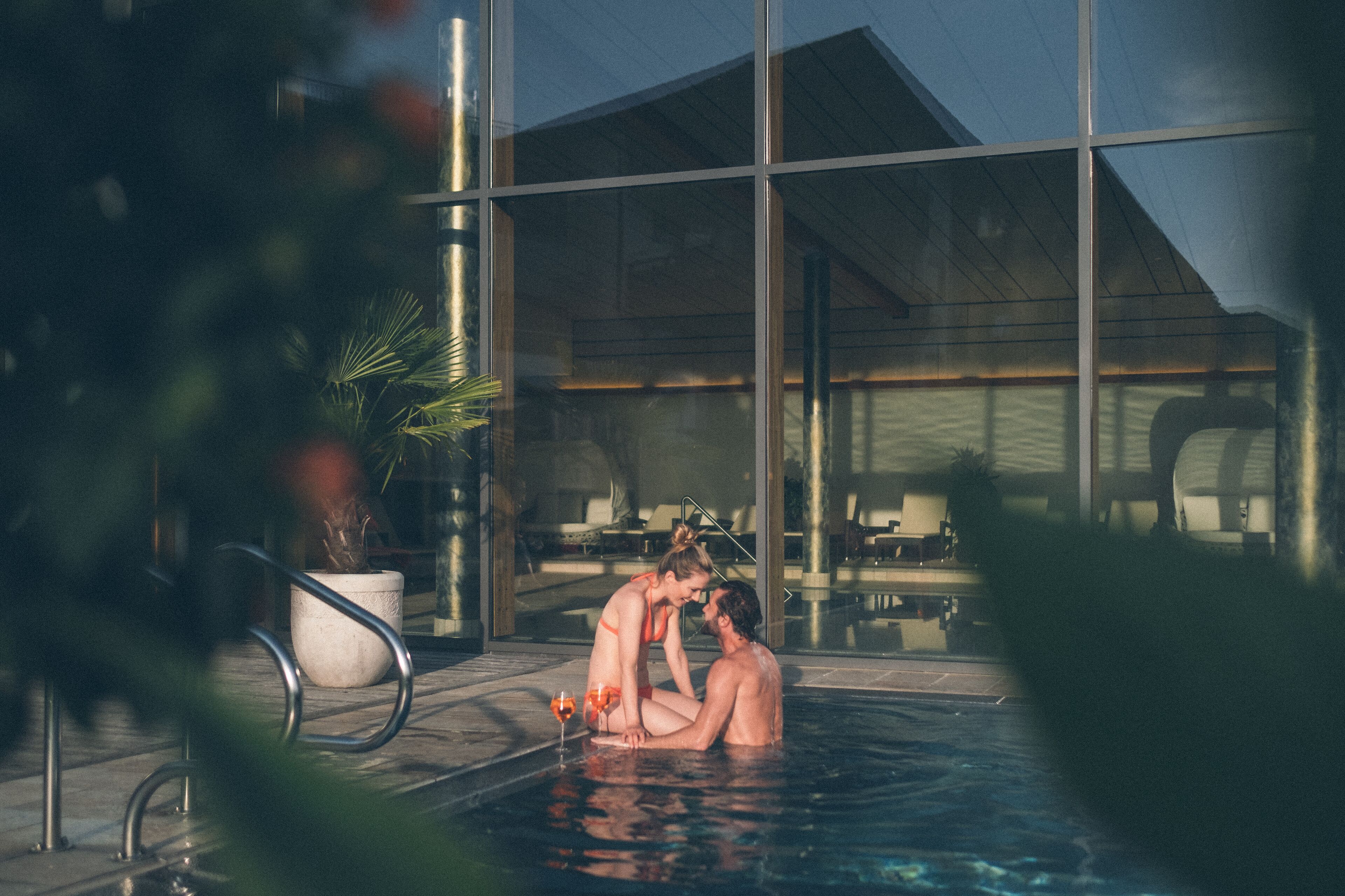 Um casal em uma piscina, com um edifício moderno ao fundo.