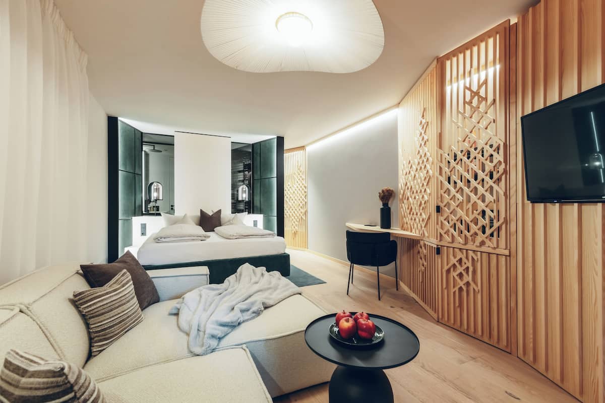 A modern hotel room with a bed, a sofa, a dining area, and a TV.