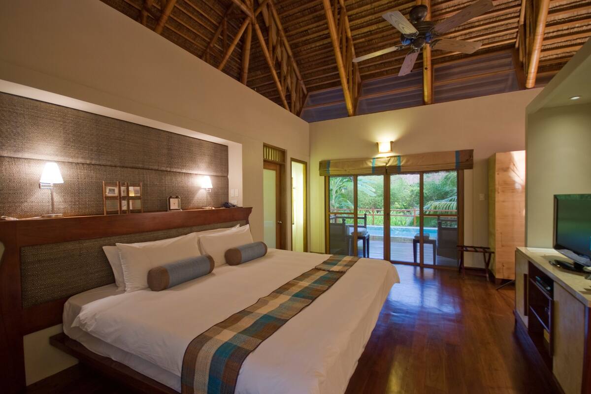 A spacious bedroom with a large bed, wooden headboard, and a ceiling fan.