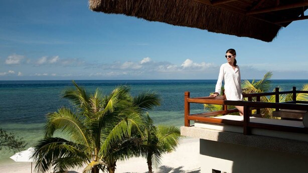 A person sitting on a wooden deck overlooking a beach with palm trees and the ocean. - Eskaya Beach Resort and Spa (Panglao)