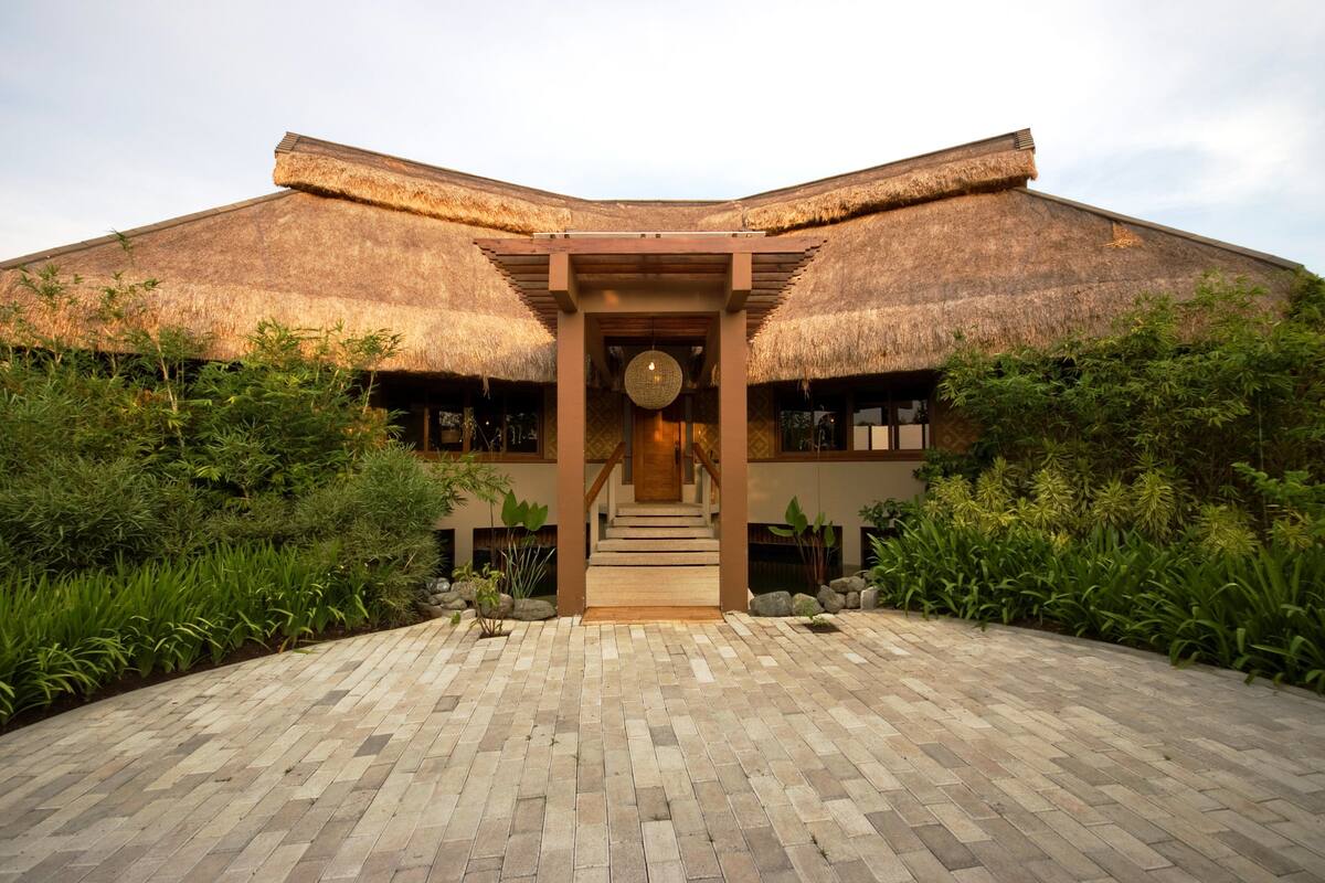 A building with a thatched roof, a central staircase, and a paved entrance area with surrounding greenery.