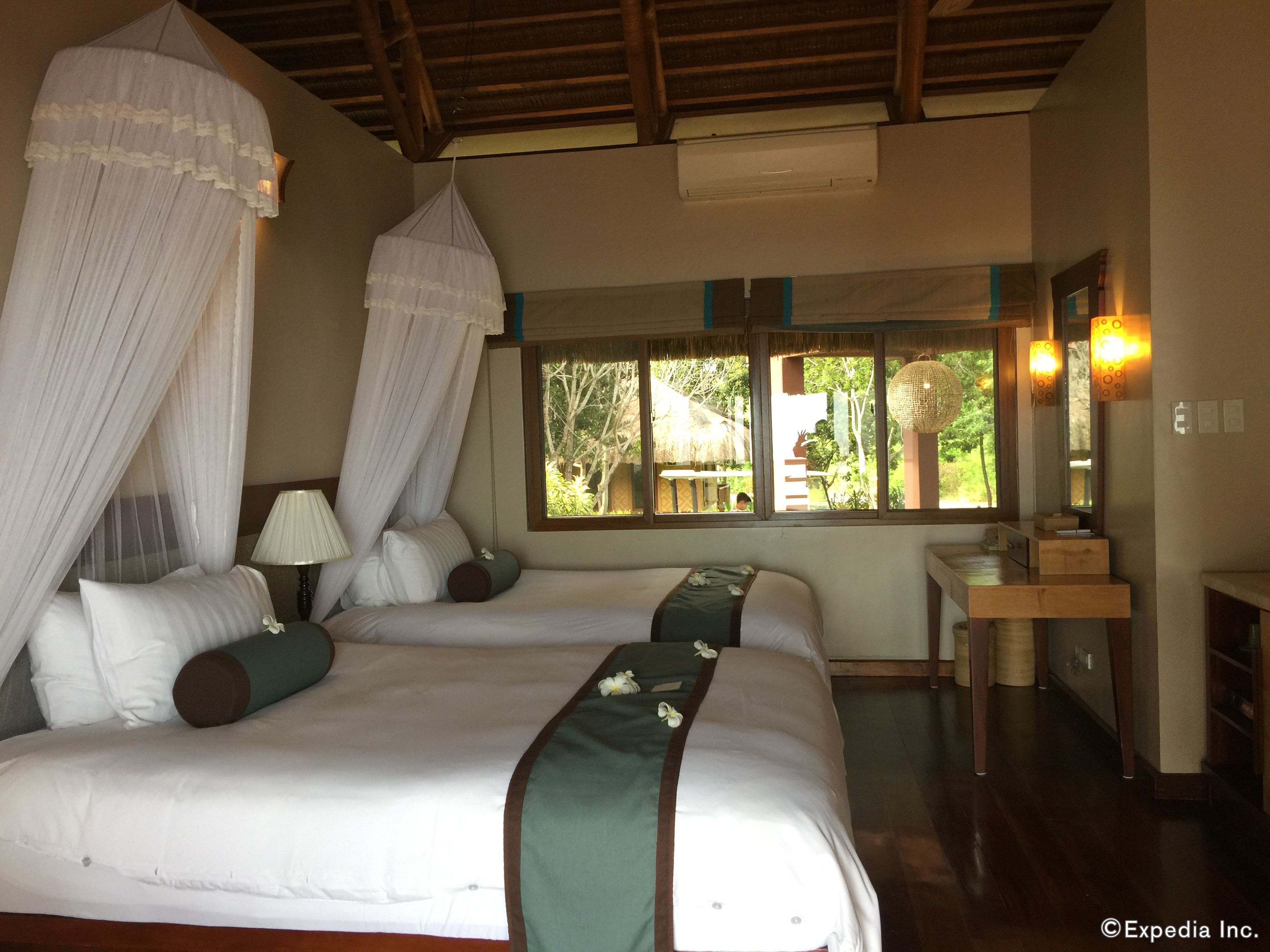 A bedroom with two beds, a window with a view of the outdoors, a bedside table, and a mirror.