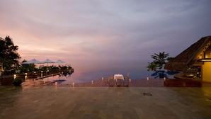 A serene evening setting with a dining table and chairs on a wooden deck overlooking a calm body of water, with a thatched-roof building and lush greenery in the background. - Eskaya Beach Resort and Spa (Panglao)