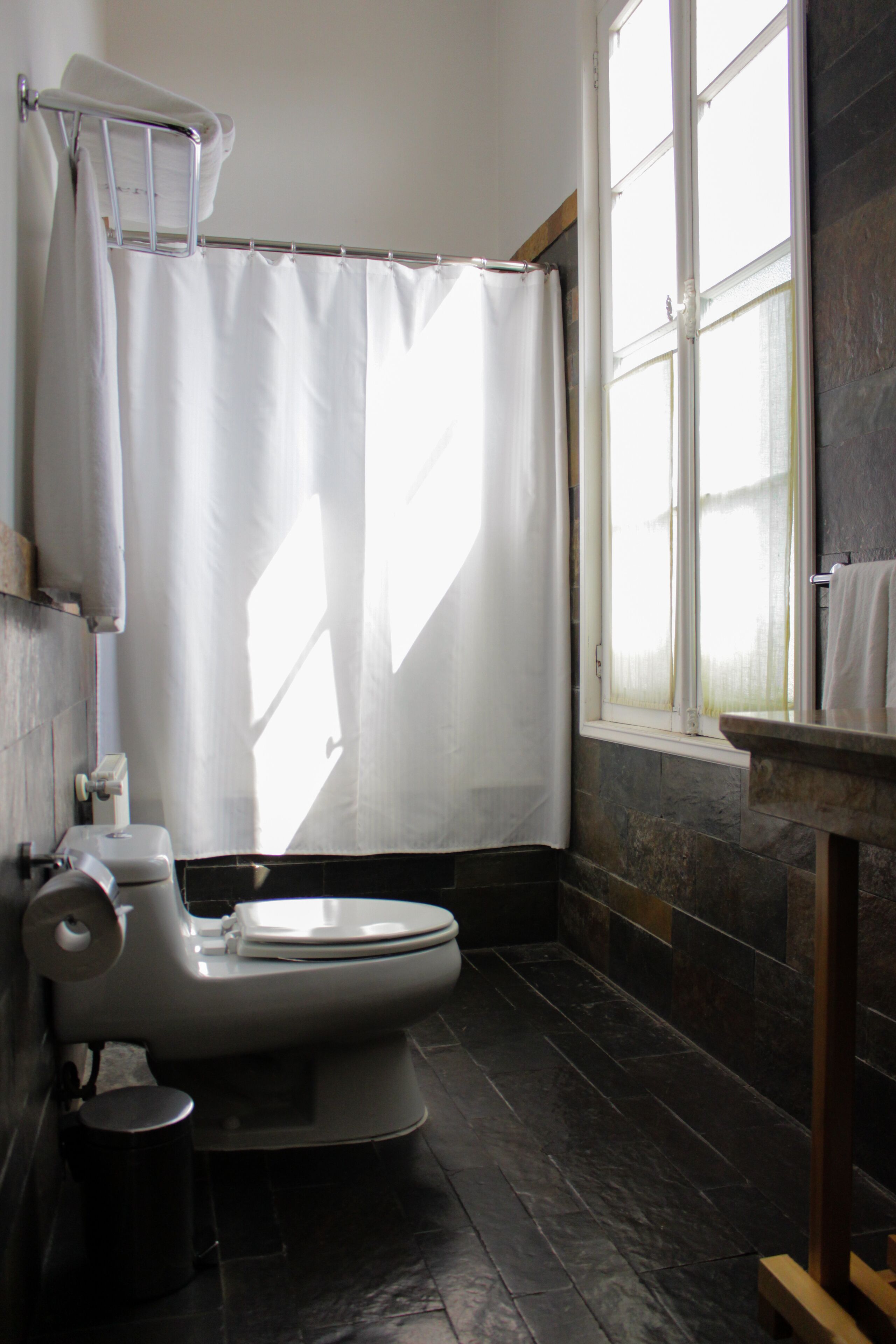 A bathroom with a toilet, a shower curtain, a window, and a stone wall.