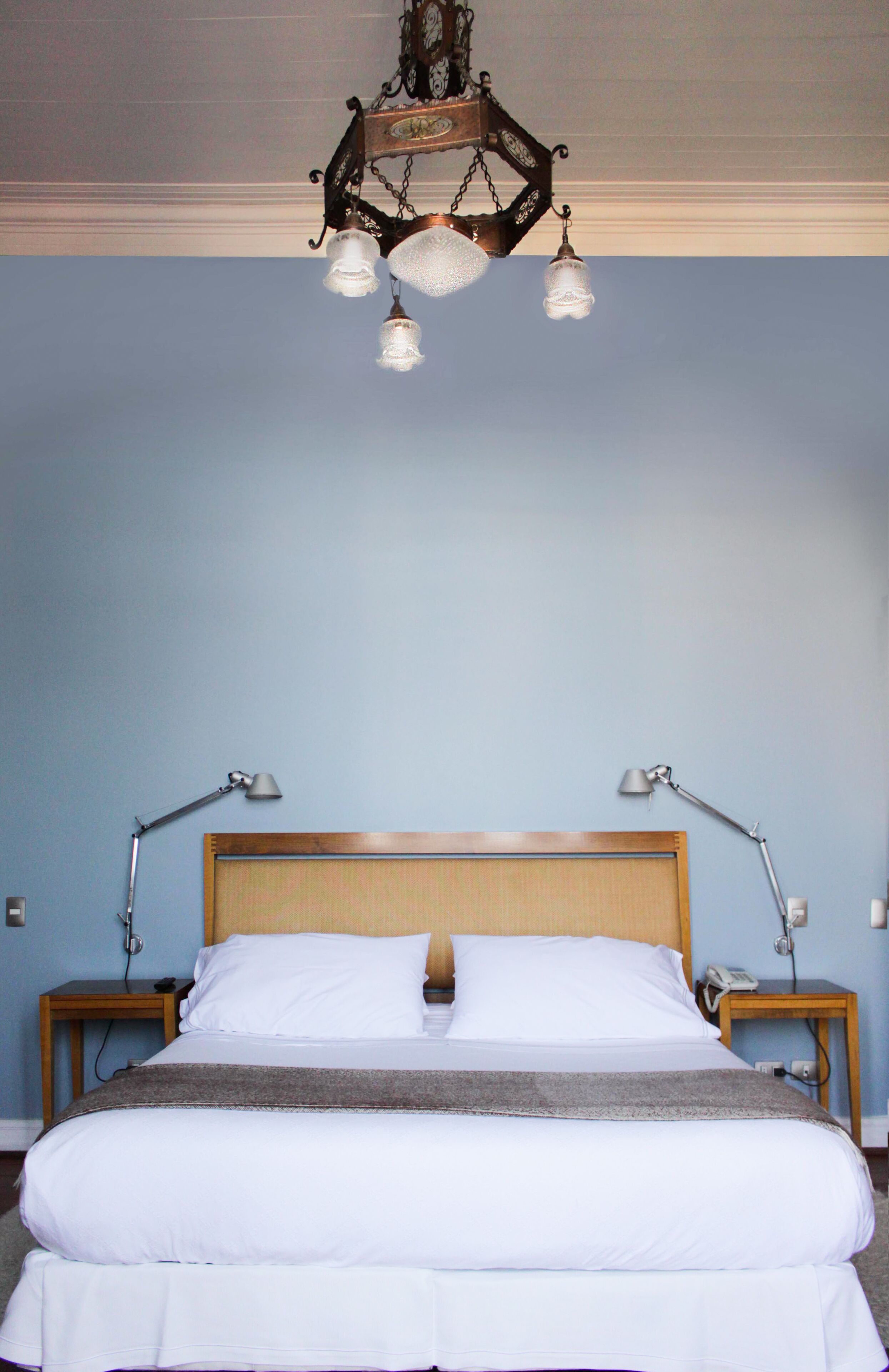 A neatly made bed with white linens, a wooden headboard, and two bedside lamps.