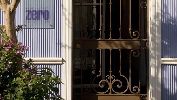 A building facade with a wrought iron balcony gate, a tree with pink flowers, and a sign that reads "ZERO HOTEL".