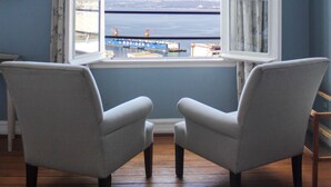 Habitación con dos sillones mirando a un ventanal grande con una persiana alzada, con vista a un cuerpo de agua y terreno lejano.