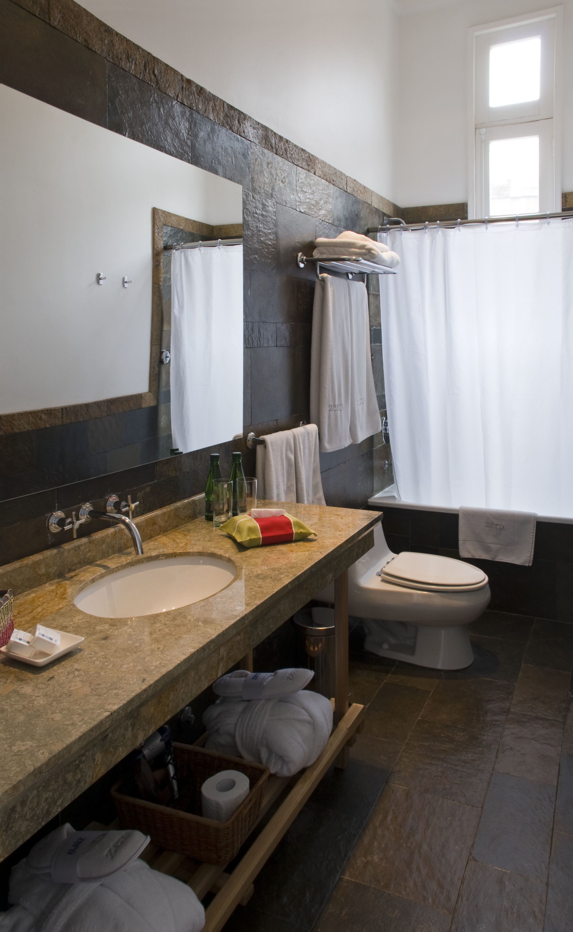 Un baño con lavamanos de encimera de piedra, un espejo, un inodoro y una cortina de ducha.