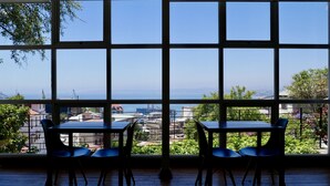 Una habitación con un ventanal amplio que ofrece vistas a la ciudad y al mar. Hay dos mesas y cuatro sillas dispuestas en la sala.