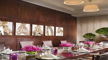 A long conference table set for a meeting with chairs, a vase of pink flowers, and a potted plant.