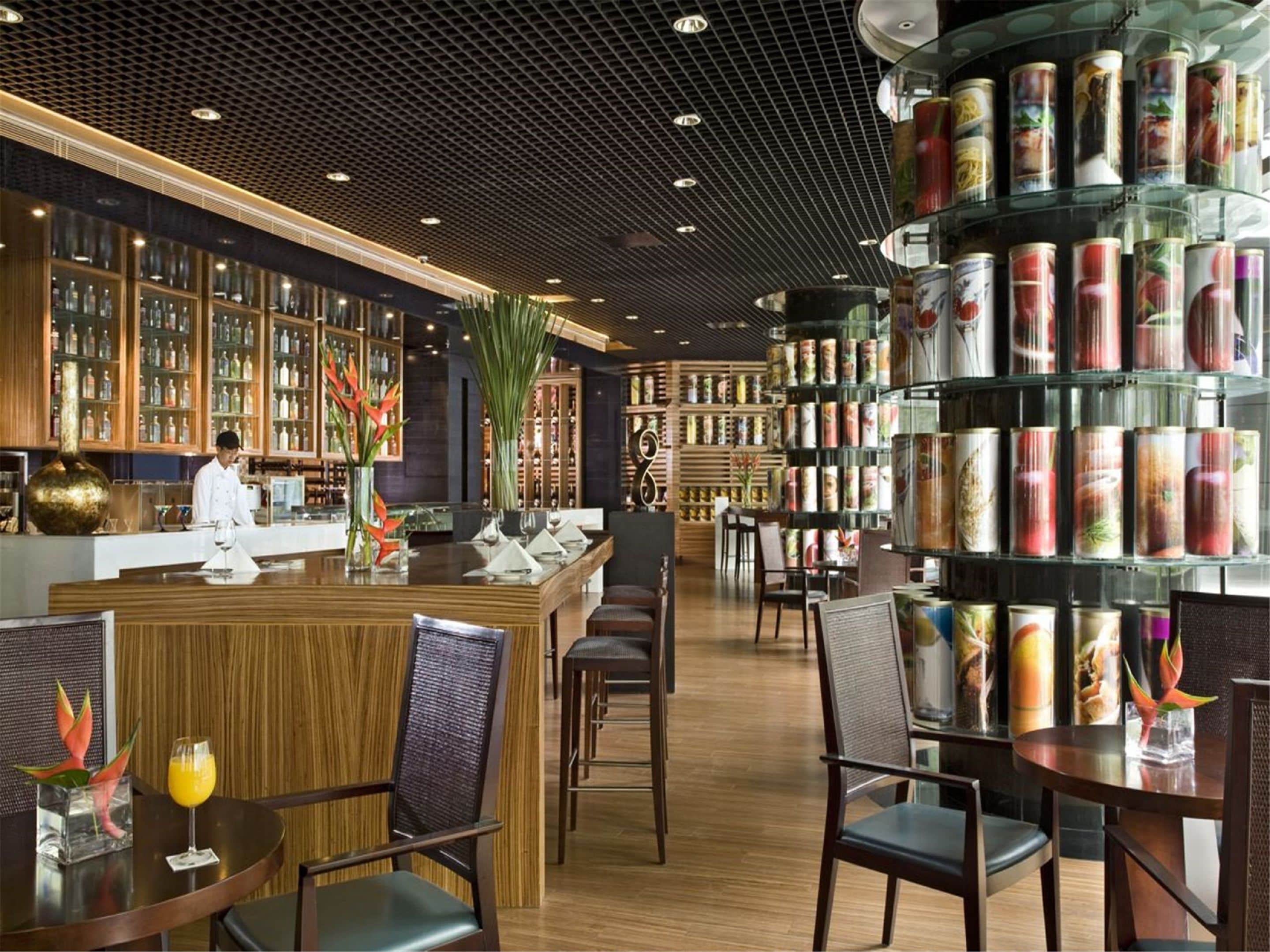 A modern bar area with wooden furniture, a bartender, and shelves stocked with canned beverages.