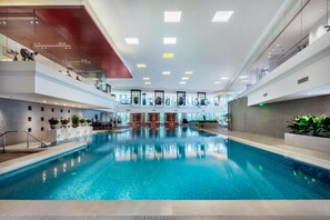 An indoor swimming pool with clear blue water, surrounded by modern architecture and glass railings. - Grand Millennium Beijing (Beijing)