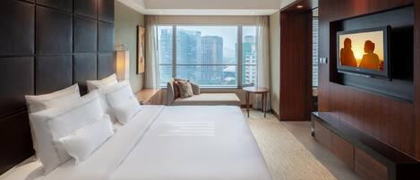 Habitación de hotel con una cama grande, un televisor montado en la pared y vistas a la ciudad desde la ventana.