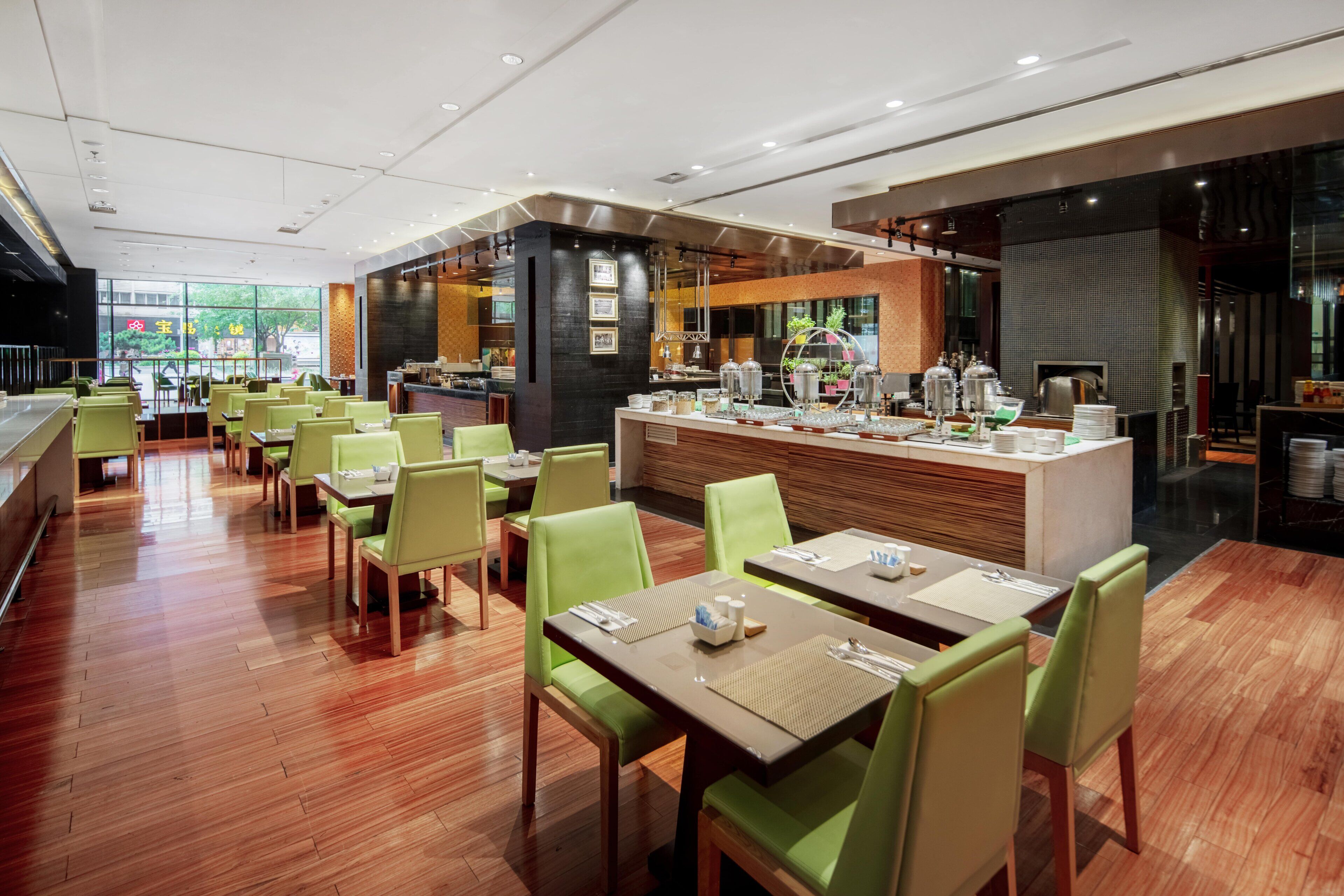 A modern restaurant with green chairs and wooden tables, a bar area, and a view of the outside.
