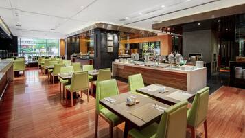 A modern restaurant with green chairs and wooden tables, a bar area, and a view of the outside.