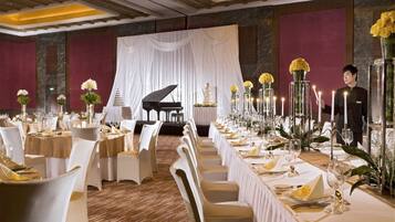 A banquet hall with long tables set for a formal event, featuring a grand piano and a tiered cake on stage.