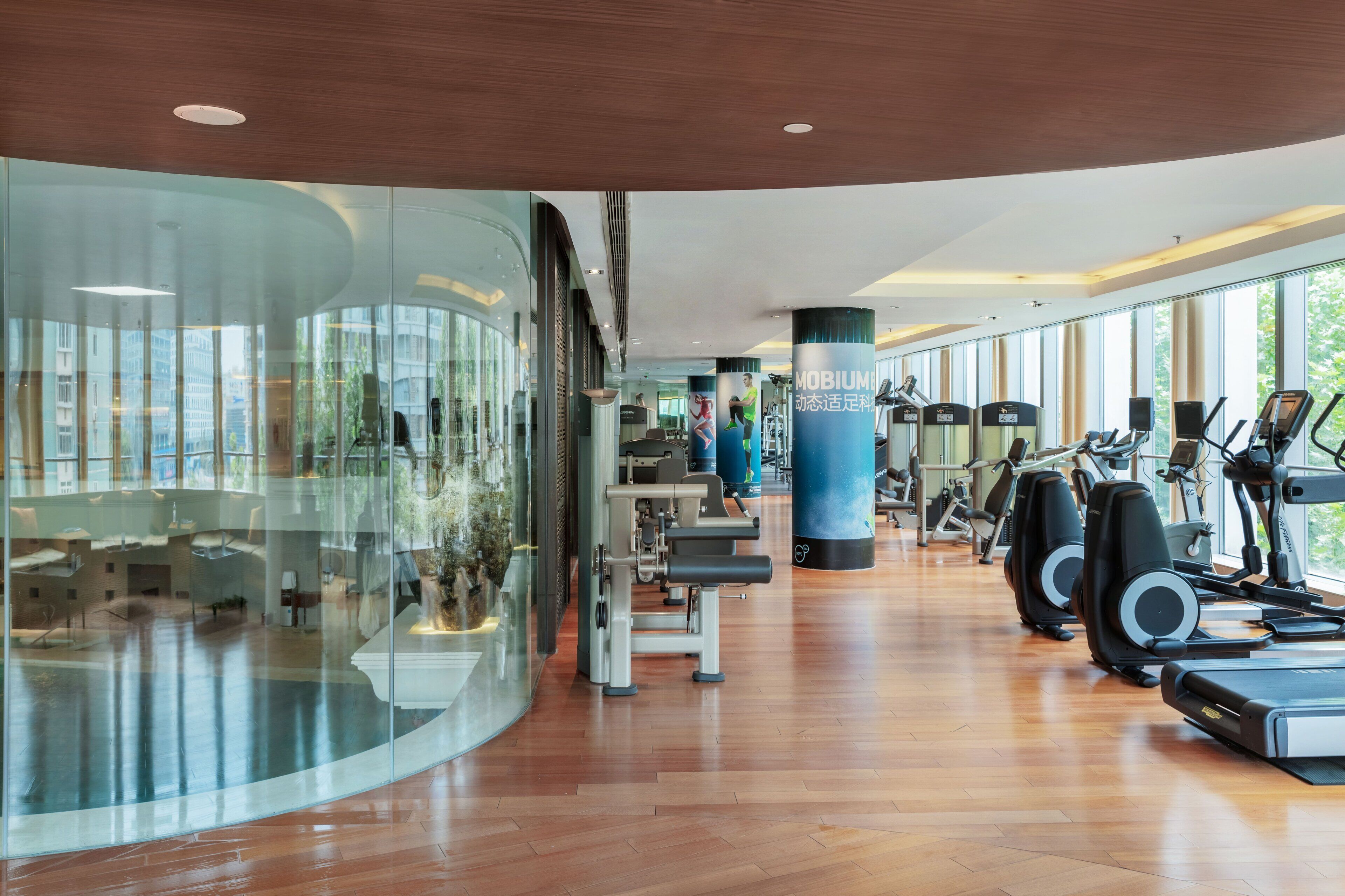 Ett modernt gym med konditionsmaskiner, styrketräningsmaskiner och en glasvägg som erbjuder utsikt över staden.
