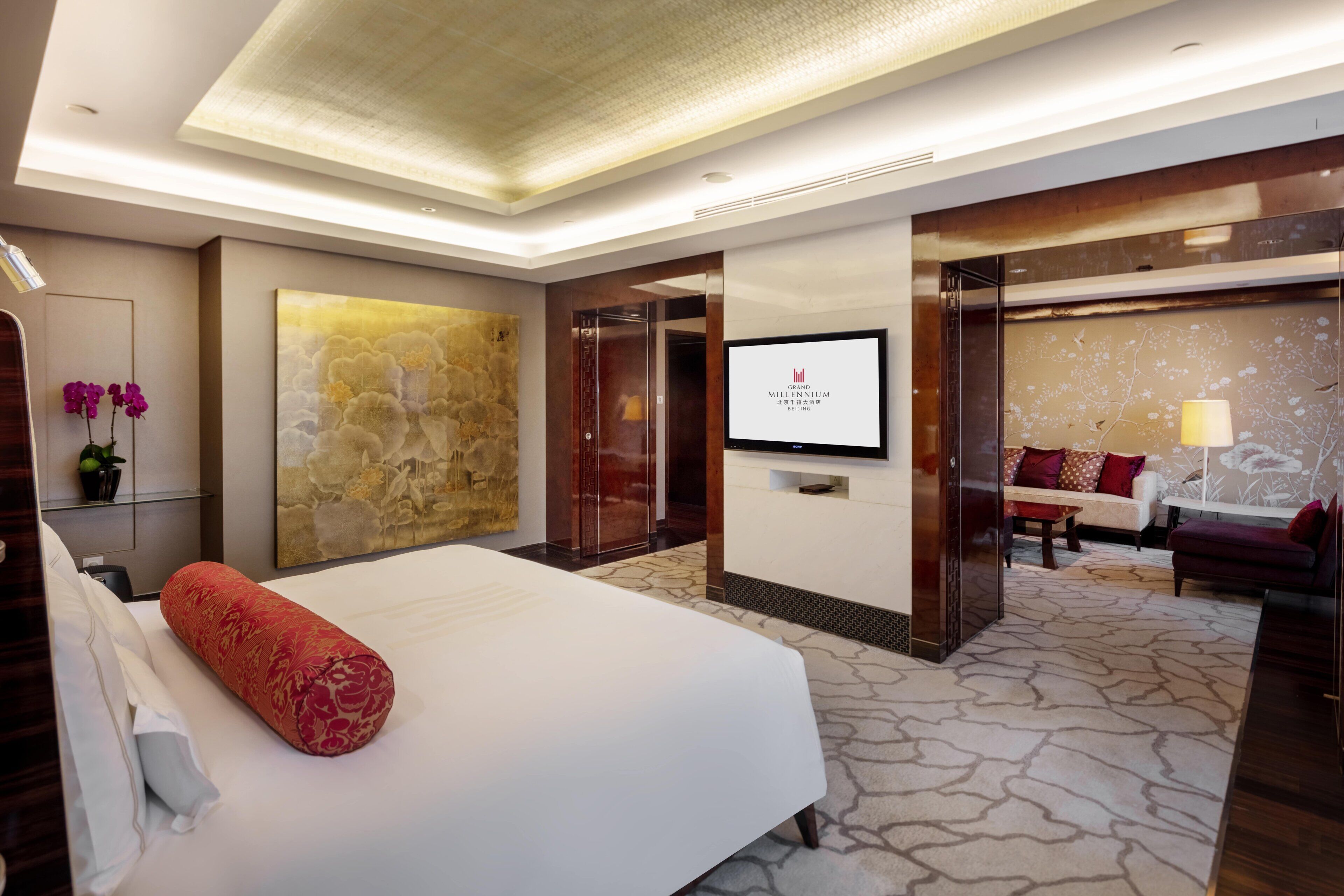 A modern hotel room with a large bed, a flat-screen TV, a stone accent wall, and a seating area with a sofa and armchairs.